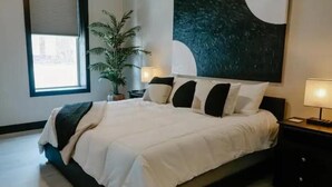 A modern bedroom with a large bed, a potted plant, and a painting on the wall.