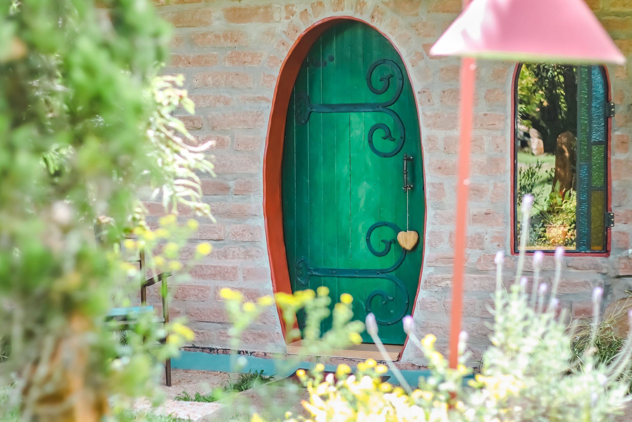 Una porta verde con una serratura a forma di cuore, incastonata in un muro di mattoni con una piccola finestra sopra.