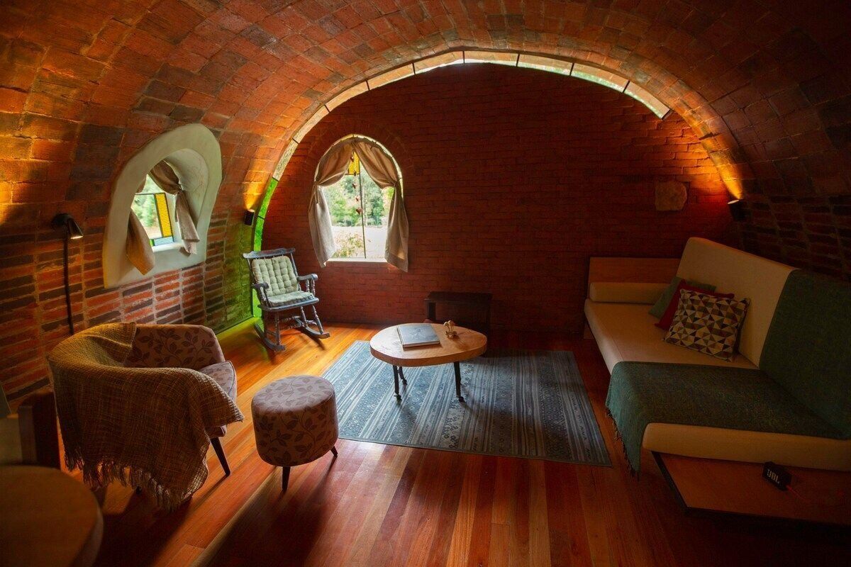 Una habitació acollidora amb un sostre d'arc de maó, un sofà verd, una taula de centre de fusta, un armari amb un disseny original i una taula petita amb una làmpada.