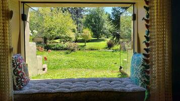 Une fenêtre donnant sur un jardin, un banc et un coussin à motifs.