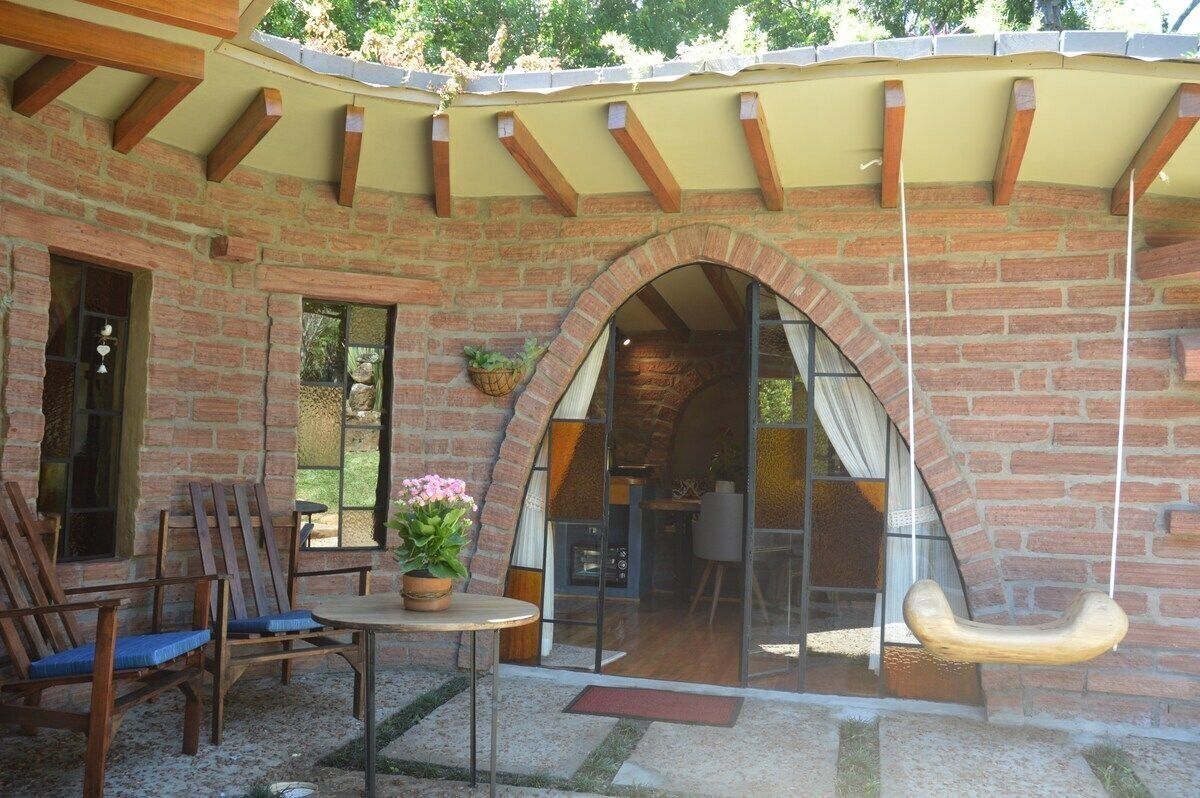 A brick patio with a swing, wooden chairs, and a table with a potted plant.