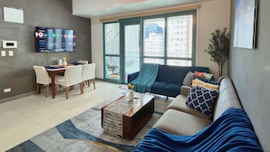 A modern living room with a sofa, coffee table, and TV mounted on the wall. - LARGE BGC 2BR, Steps to Mitsukoshi & Uptown Malls, 300Mbps Fiber 25R (Taguig)
