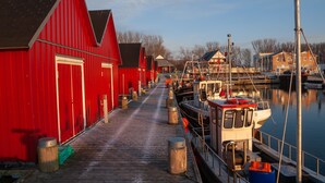 Eine Holzsteganlage, die zu einer Reihe roter Gebäude führt, vermutlich ein Yachthafen oder Hafen.