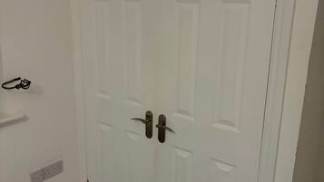 Una puerta blanca con picaporte y cerradura, un enchufe en la pared y una pequeña estantería.