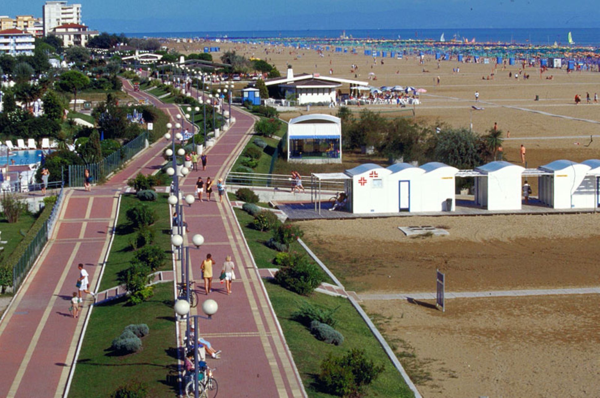 A beachside promenade with a running track, beach umbrellas, and beachgoers.