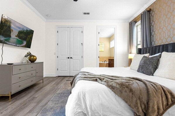 Une chambre à coucher avec un grand lit, une commode, un tableau et une porte donnant sur une salle de bain.