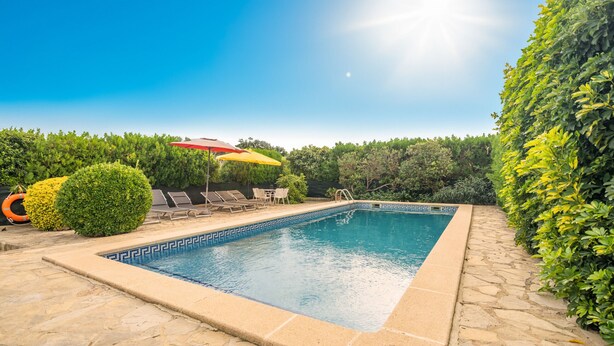 Una piscina rectangular con un borde de mosaicos decorativos, rodeada de suelo de piedra.