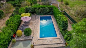 Une piscine rectangulaire bordée de pierres, entourée d’une végétation bien entretenue et d’un chemin en pierre.