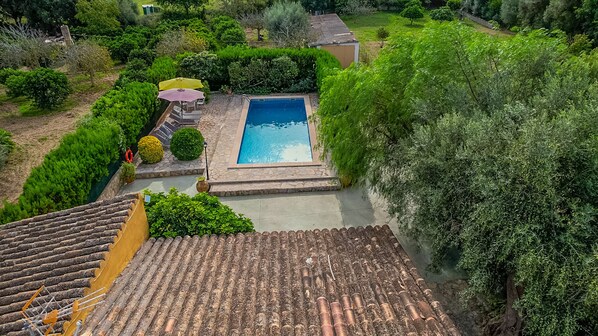 Une piscine sur le toit, bordée de pierres, entourée d’une végétation luxuriante et surmontée d’un toit en tuiles.