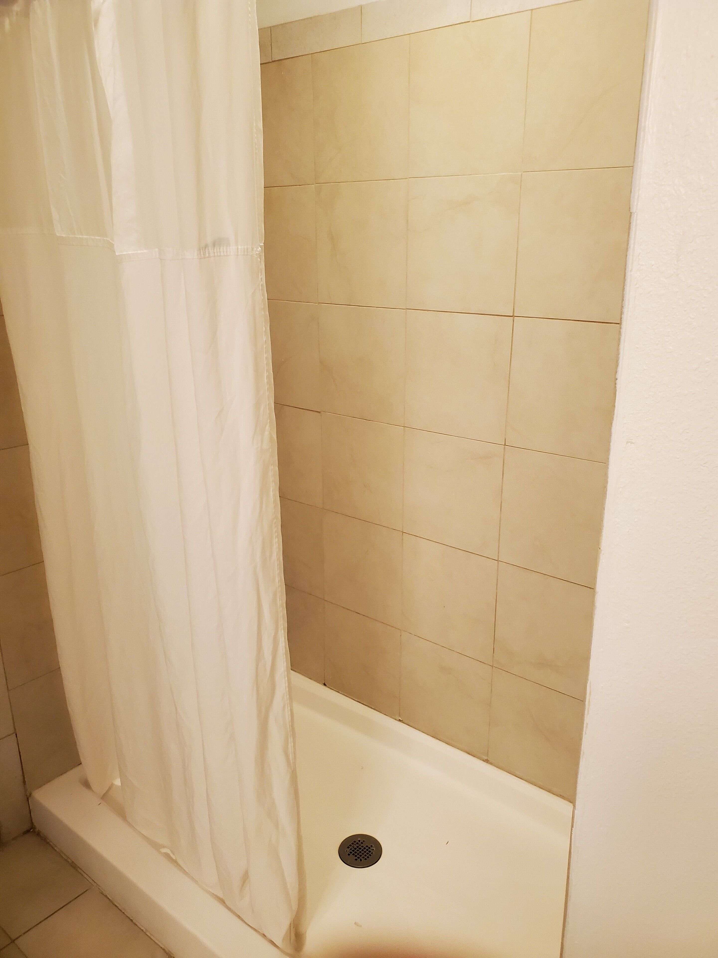 Een badkamer met een douchegedeelte, betegelde wanden en een afvoer in de douche.