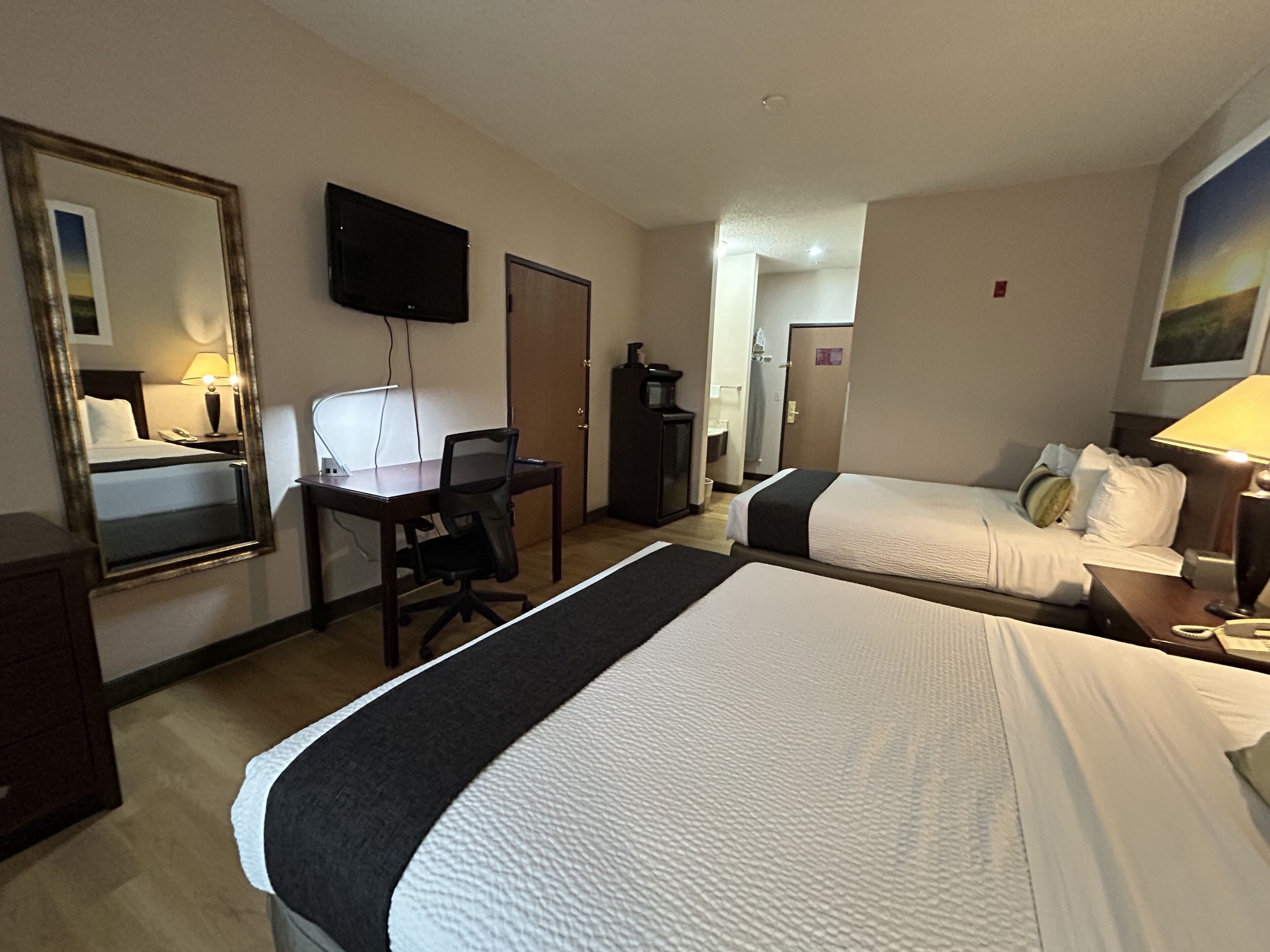 Habitación de hotel con dos camas, un escritorio, una silla, un televisor y un espejo.