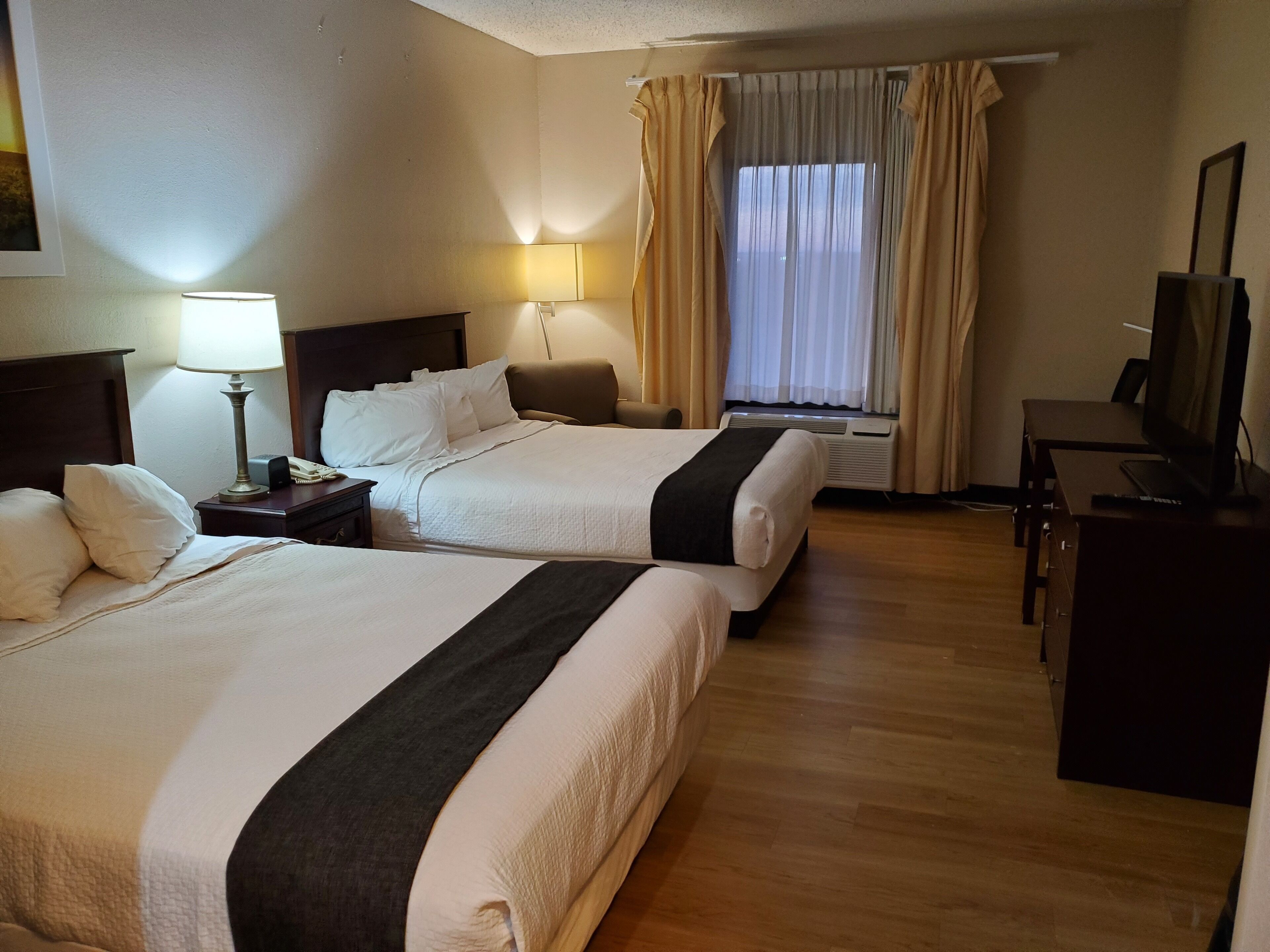 A hotel room with two beds, a desk, a chair, a TV, and a window with curtains.
