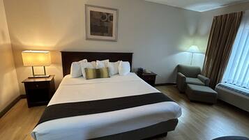 A hotel room with a large bed, a chair, a desk, a lamp, and a picture on the wall.