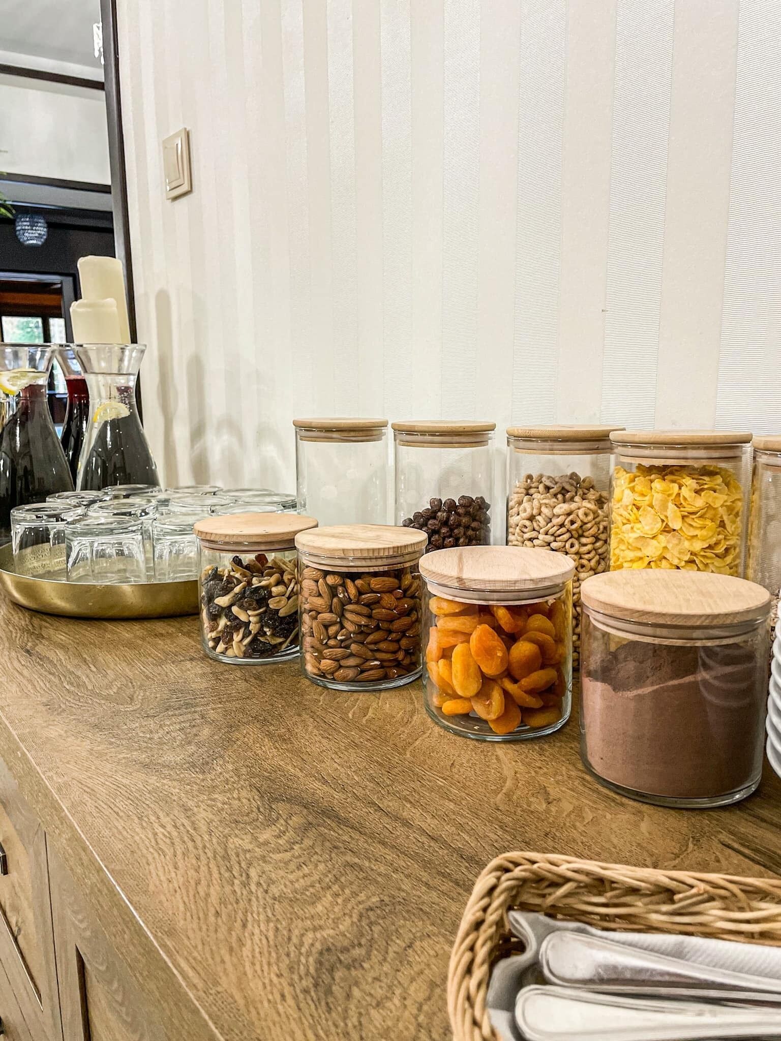 A wooden counter with glass jars containing various nuts, dried fruits, and chocolate powder.