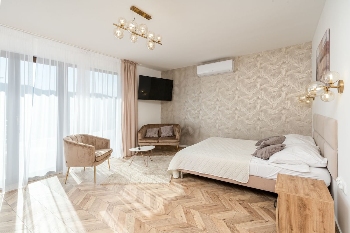 A modern bedroom with a large bed, a sofa, a TV, and a wooden floor.