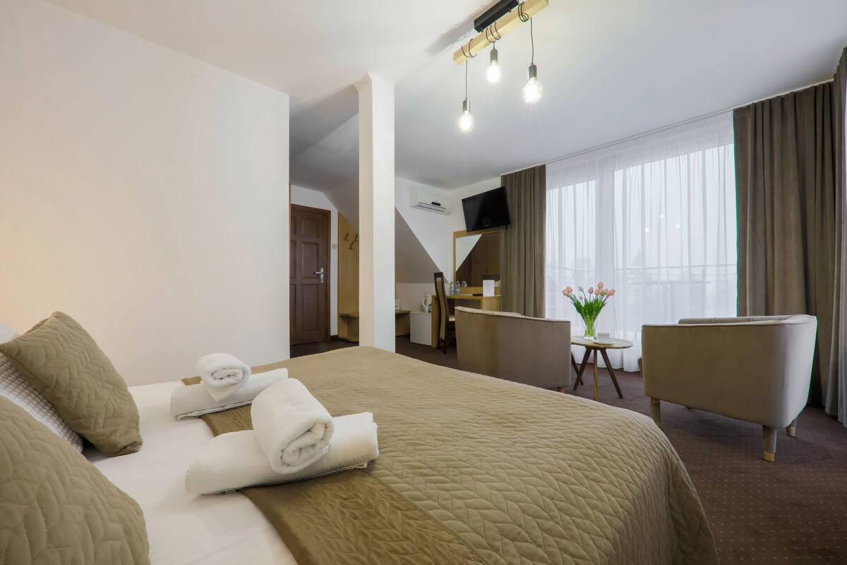 A hotel room with a large bed, a sitting area with a chair, a small table, and a mirror.