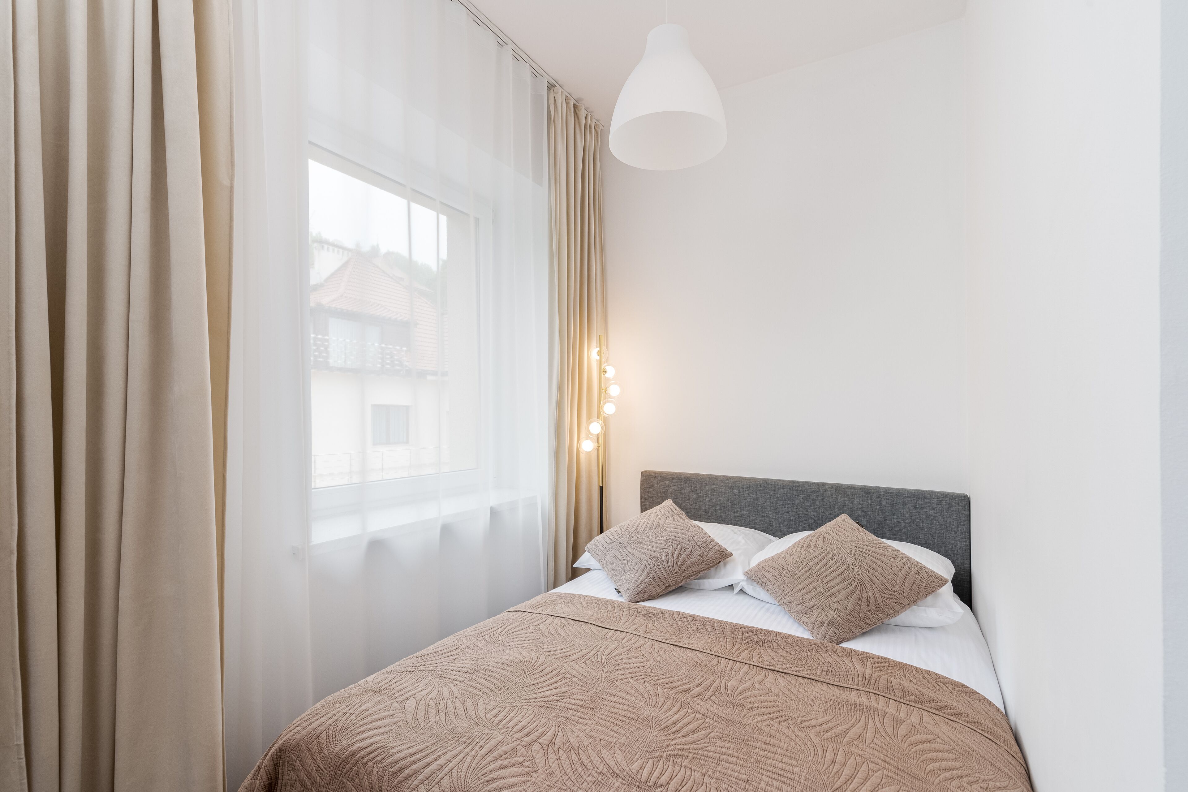 A neatly made bed with a patterned bedspread, a grey headboard, and two pillows.