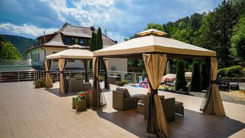 A covered outdoor seating area with wicker furniture and a pool in the background.