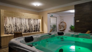 A spa area with a large hot tub, wooden wall decor, and a wicker chair. - Hotel Łaziska (Czchow)