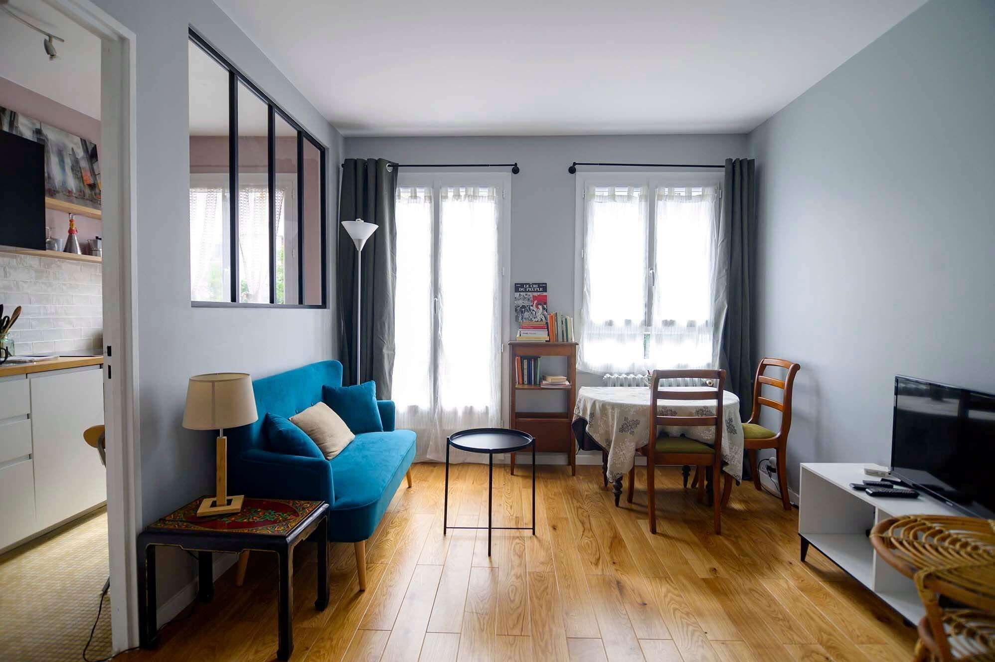 Un salon avec un canapé bleu, une petite table, une bibliothèque, une table à manger avec des chaises et un téléviseur.