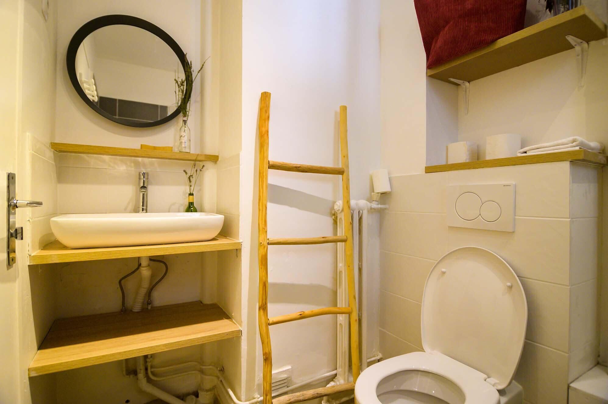 Une salle de bain avec un lavabo blanc, un miroir, des toilettes et une échelle en bois.