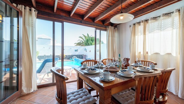 Un comedor con una mesa de madera dispuesta para cuatro, una piscina visible a través de puertas de vidrio y vistas al área de la piscina exterior.