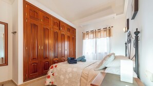 Un dormitorio con un armario grande, una cama con colcha estampada y una mesita de noche con lámpara.