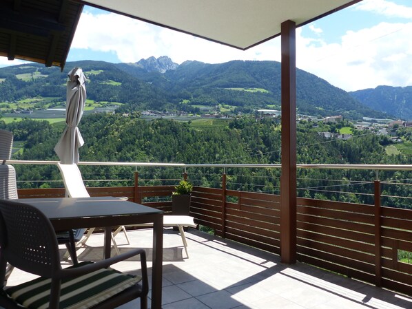 En balkong med ett bord och stolar, med utsikt över ett bergigt landskap och en by nedanför.