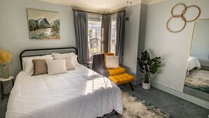 Une chambre à coucher avec un lit, une fenêtre avec des rideaux, un miroir et une plante.