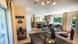 Un salon moderne avec une cheminée, un panneau indiquant un bar à café et un coin repas avec une table et des chaises.