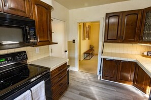 Une cuisine avec des meubles de rangement en bois, un micro-ondes noir, une cuisinière et un dosseret carrelé.