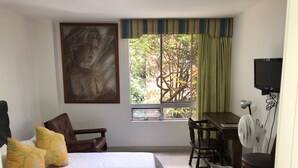 A bedroom with a bed, a desk, a chair, a TV, and a window with a view of trees.