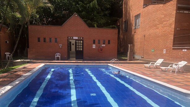 A swimming pool with a depth sign of 1.25 meters, surrounded by a brick building with a door and windows, and a few lounge chairs.