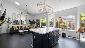 A modern kitchen with a central island, dark cabinetry, and pendant lighting. - Botany House Designer Home with Hot Tub (Santa Rosa)