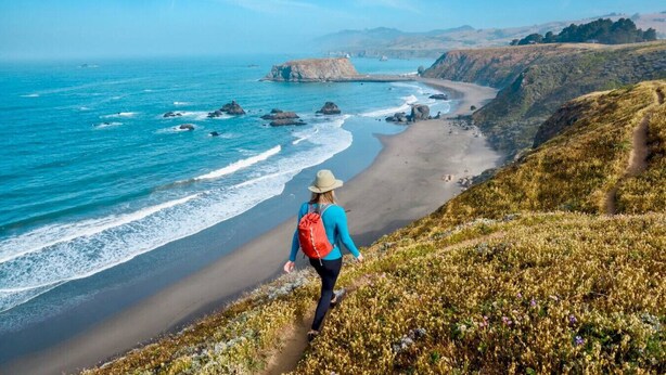 A person hiking along a coastal path with a view of the ocean and cliffs. - Botany House Designer Home with Hot Tub (Santa Rosa)