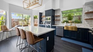 Une cuisine moderne dotée d’un îlot central, de meubles de rangement aux couleurs sombres et d’une grande fenêtre offrant une vue sur l’extérieur.