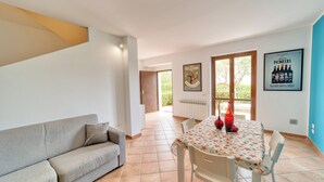 A modern living room with a sofa, a dining table with chairs, and a kitchen area visible through an open door. - Stagnone Wine House (Marsala)