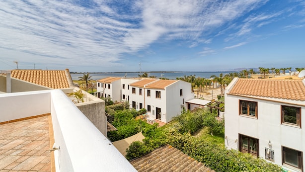 A coastal residential area with terracotta-tiled roofs, white buildings, and a view of the sea. - Stagnone Wine House (Marsala)