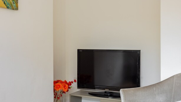 A modern living room with a flat-screen TV on a stand, a grey sofa, a patterned rug, and a vase with orange flowers. - PickThePlace Kensington Lux Apartments II (London)