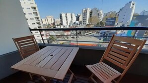 Un balcone con un tavolo di legno e due sedie, affaccia su un panorama urbano con edifici e un cantiere edile.