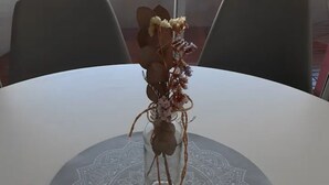 Un tavolo con un vaso di vetro contenente fiori secchi e un oggetto decorativo.