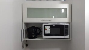 Un microondas y una cafetera sobre un estante blanco dentro de un armario de cocina.