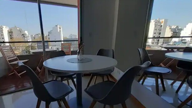 Zona pranzo moderna con tavoli e sedie rotonde, ampie finestre vista città e un balcone con ringhiera.