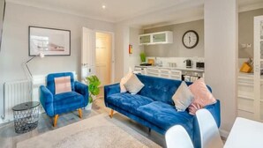 A modern living room with a blue sofa, a small round table, and a white dining table. - Molokai Snug | Best location | North South bay | Courtyard garden | Parking (North Yorkshire)