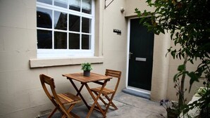 A small wooden table and chairs set against a beige wall, with a window above and a door to the right. - Molokai Snug | Best location | North South bay | Courtyard garden | Parking (North Yorkshire)