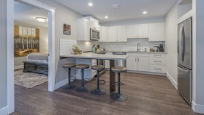 Eine moderne Küche mit weißen Schränken, einem Edelstahlkühlschrank und einer Bar mit Barhocker.