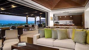 A modern living room with a sofa, coffee table, and dining area. A kitchen is visible in the background.