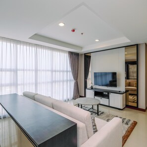 A modern living room with a sofa, a coffee table, a TV, and a large window with sheer curtains. - Brand New 2Br Apartment At The Kencana Residence (Jakarta)