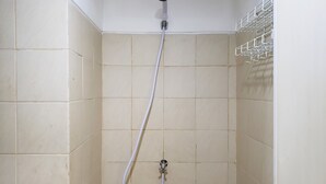 Une douche équipée d’un pommeau flexible, de carreaux de couleur beige et d’une étagère métallique fixée au mur.