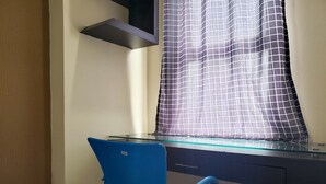 Une pièce comprenant un bureau, une chaise, une fenêtre avec un rideau à motifs et une étagère fixée au mur.